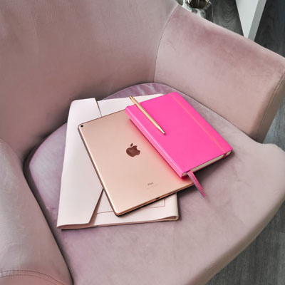 A pink notebook and an apple ipad sitting on top of a chair.