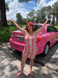 A woman standing next to a pink car.