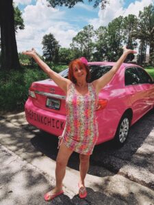 Pink Chick Psychic is excited standing by her hot pink Toyota Corolla